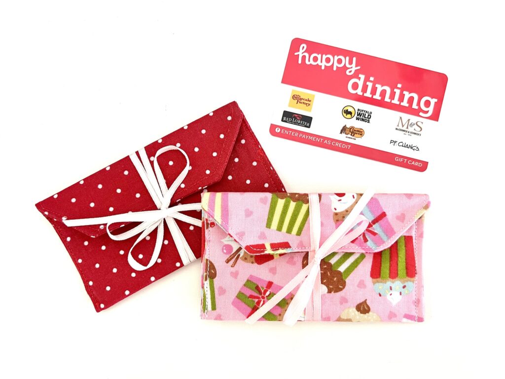 Two fabric gift card holders, one red with white polka dots and one pink with a dessert pattern, are placed next to a “Happy Dining” gift card.