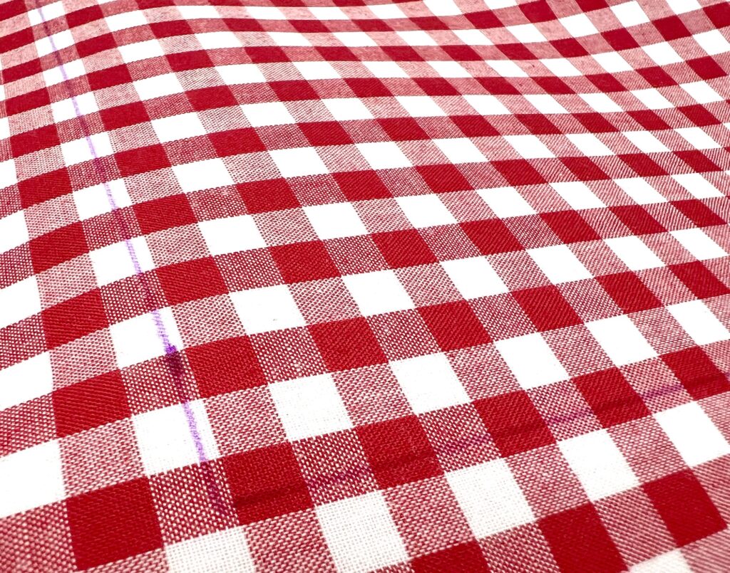 Red and white checkered tablecloth with a woven texture, laid out flat and viewed from an angle.