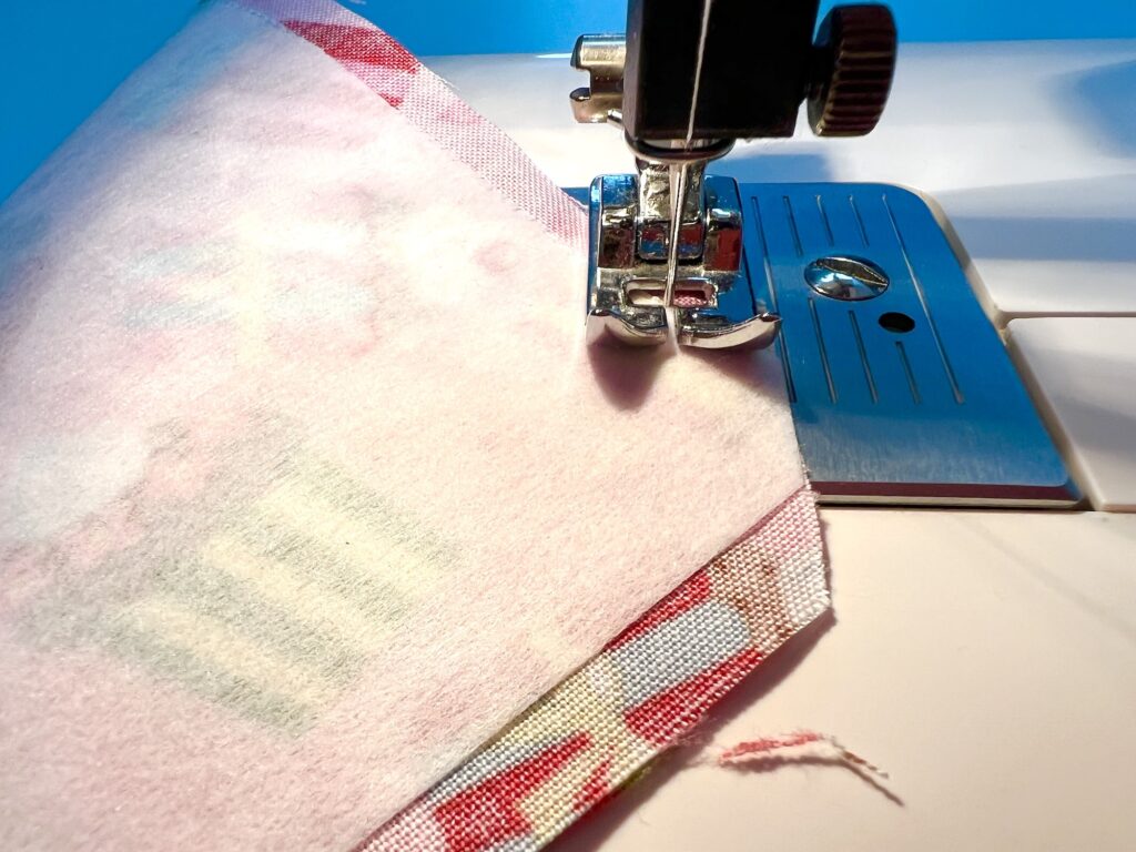 Close-up of a sewing machine stitching two pieces of fabric together, with the presser foot holding the material in place.