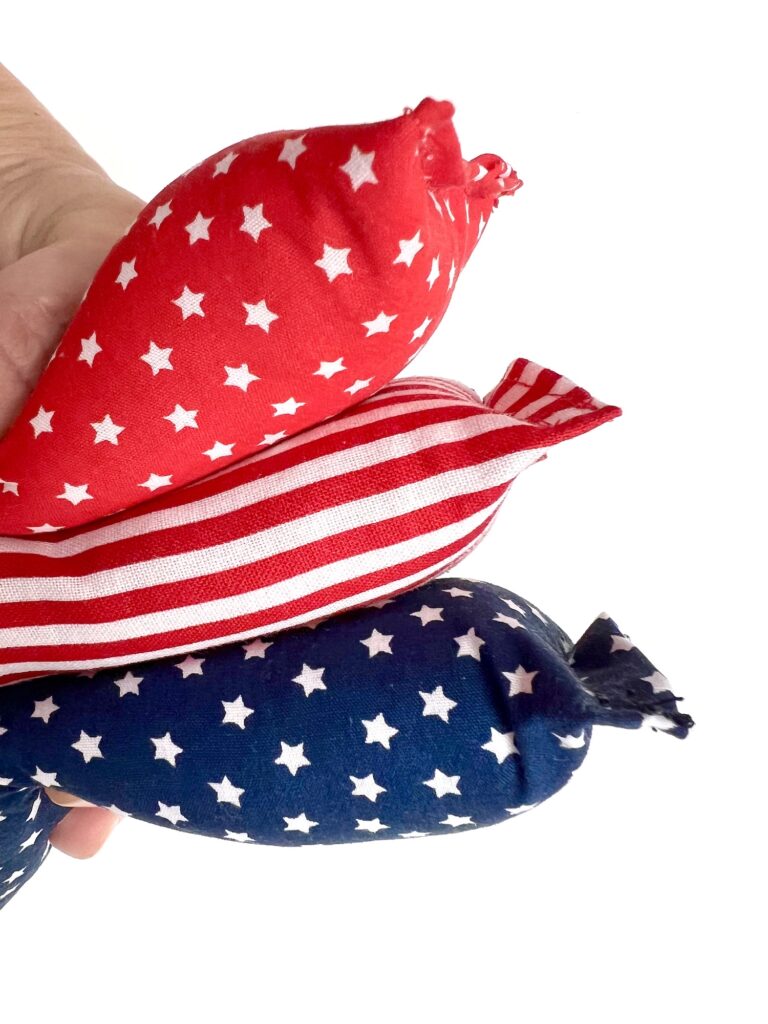A hand holds three fabric items in red, white, and blue patterns with stars and stripes, resembling the American flag.