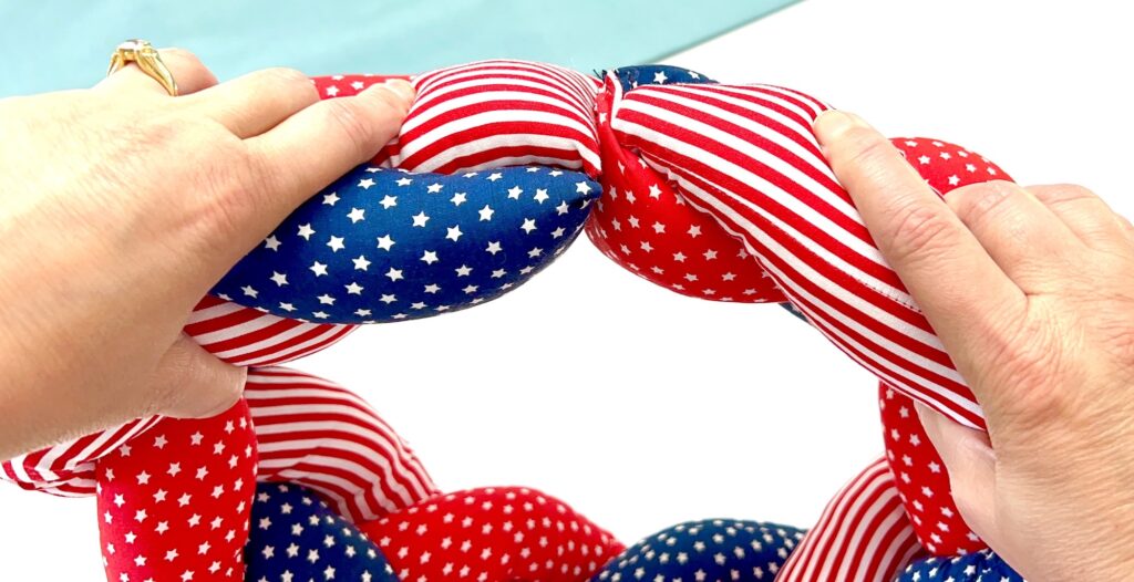 Close-up of hands holding a braided fabric ring with red, white, and blue star and stripe patterns on a white background.