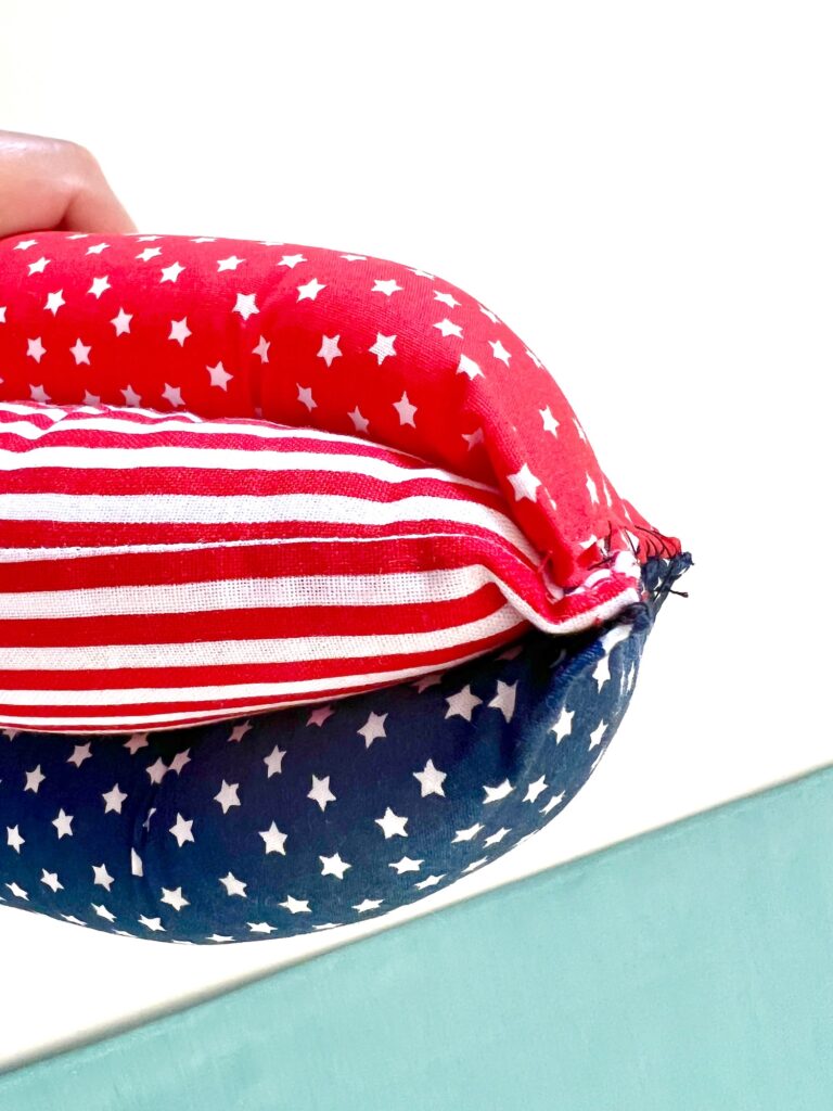 A hand holds a bean bag with red, white, and blue fabric featuring stars and stripes, resembling the American flag.