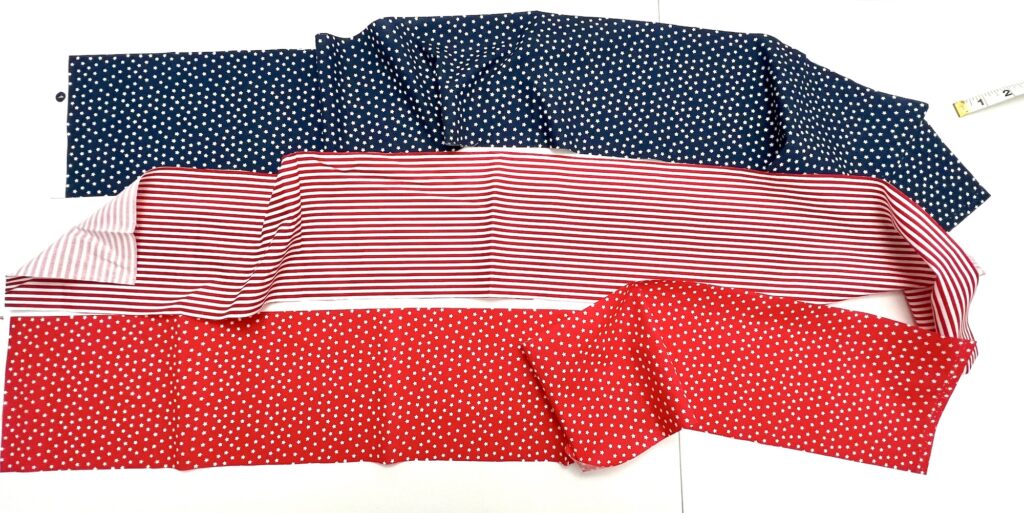 Three pieces of patterned fabric are laid out: one dark with white dots, one white with red stripes, and one red with white dots. A measuring tape is visible in the top right corner.