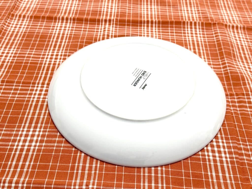 A white plate is placed upside down on an orange and white checkered tablecloth. The underside label is visible.