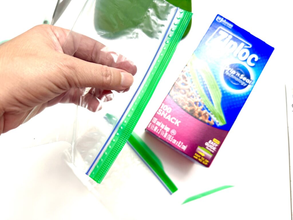 A hand uses a Ziploc plastic bag with a green zipper seal like a pot holder, holding it above a box of Ziploc storage bags against a white background.