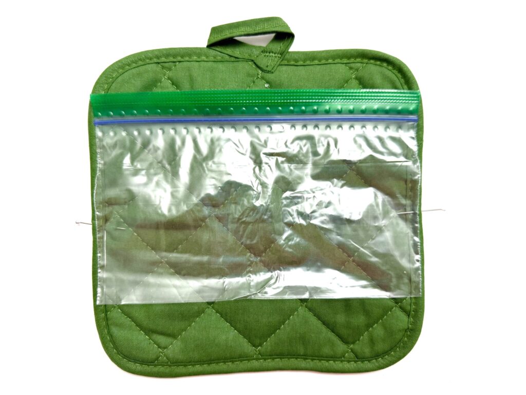 A clear resealable plastic bag rests on a green quilted pot holder with a hanging loop, against a white background.