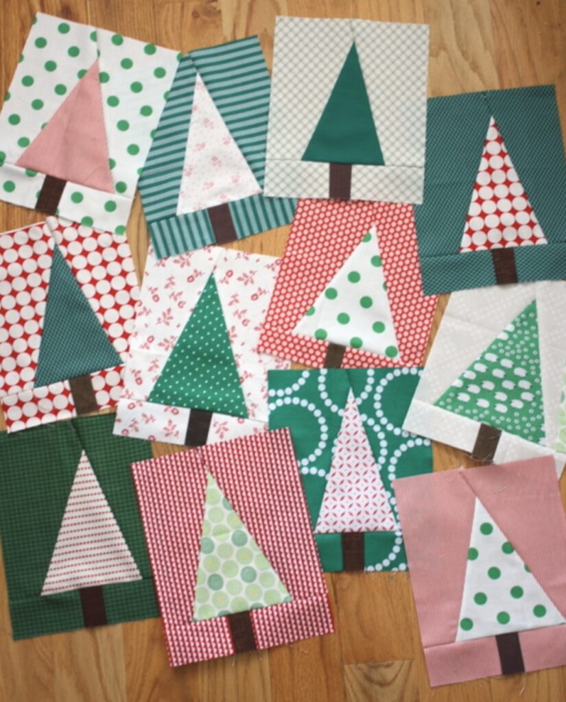 Several quilt blocks featuring stylized Christmas tree designs in various fabrics and colors are arranged on a wooden floor.