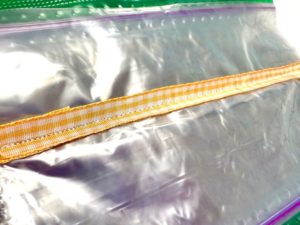 Close-up of clear plastic zip lock bags stacked together with a yellow and orange ribbon placed across them, next to a colorful pot holder.