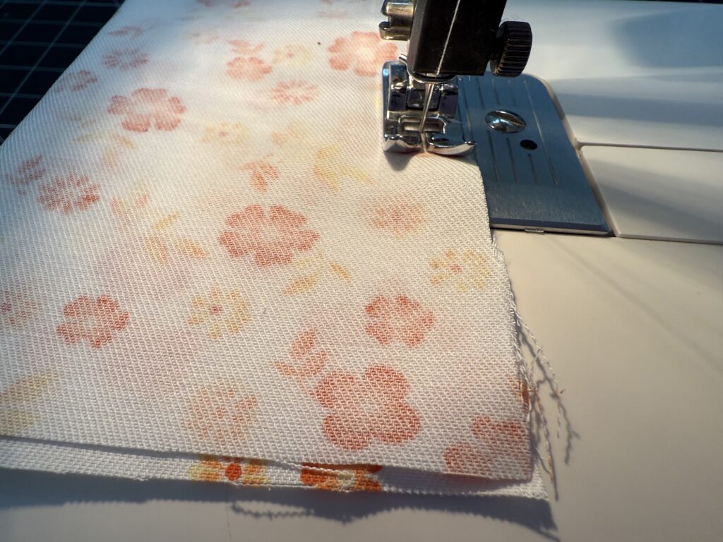 Close-up of a sewing machine stitching together two pieces of white fabric with a pink and yellow floral pattern.