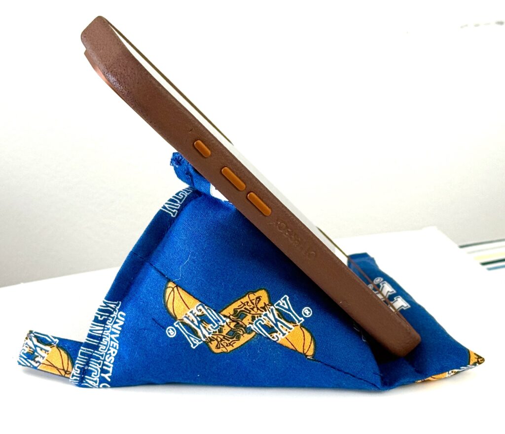 A smartphone with a brown case rests on a blue fabric pyramid stand featuring a University of California logo, making it a perfect example of fun teen sewing projects.