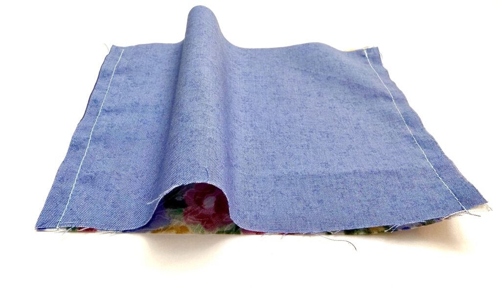 A piece of blue fabric with two stitched seams on each side, partially raised in the center, placed on a white surface.