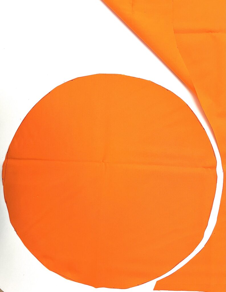 An orange fabric circle and scraps on a white background, with the fabric showing fold lines and slight wrinkles.