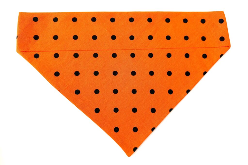 An orange triangular over the collar dog bandana with black polka dots, laid flat on a white background.