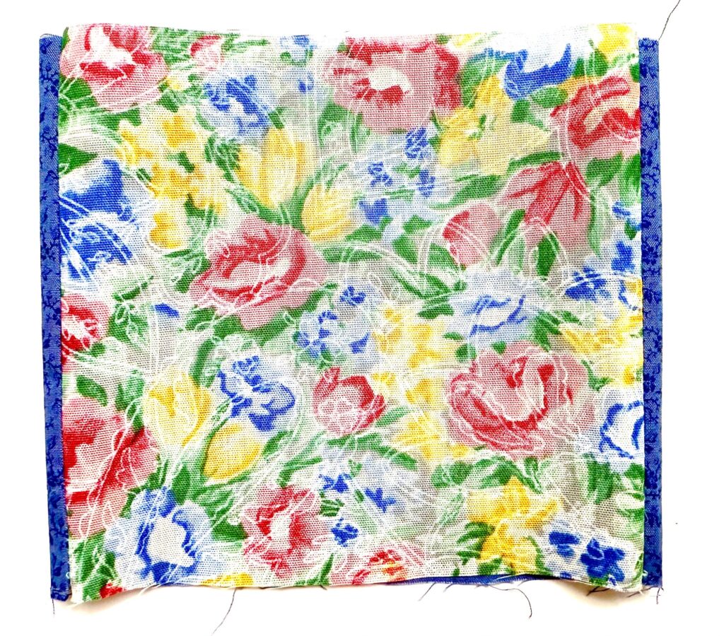A square piece of floral fabric with a pattern of red, yellow, and blue flowers and blue borders on the left and right edges.