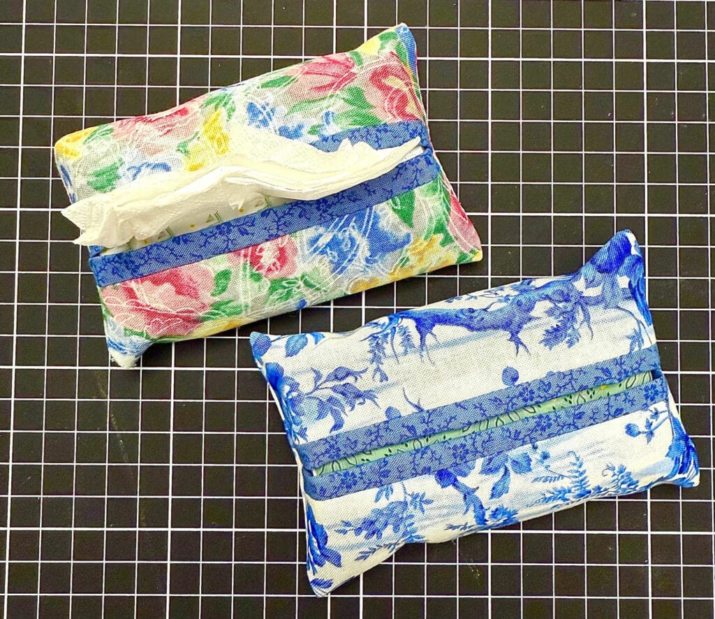 Two rectangular tissue holders with floral patterns, one in blue and white and the other multicolored, are placed on a black grid surface.
