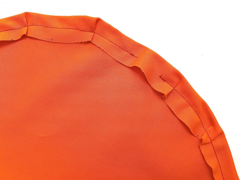 Close-up of the edge of an orange fabric with visible stitching and folded seam allowances, perfect for crafting a festive Halloween wreath.