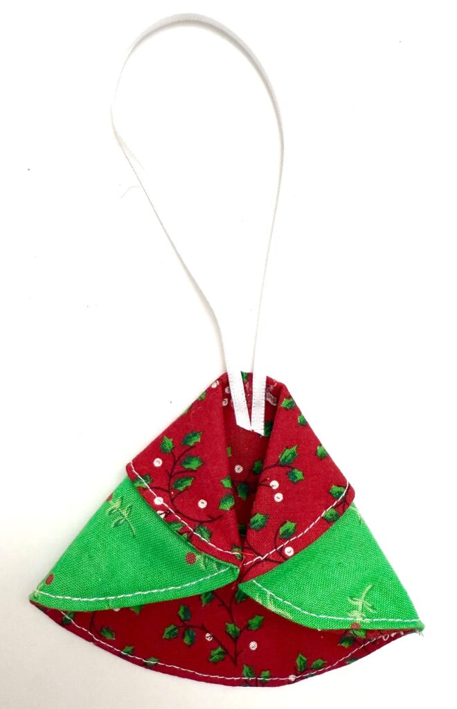 A handmade fabric ornament with red and green patterned cloth, white stitching, and a white hanging loop, displayed on a white background.