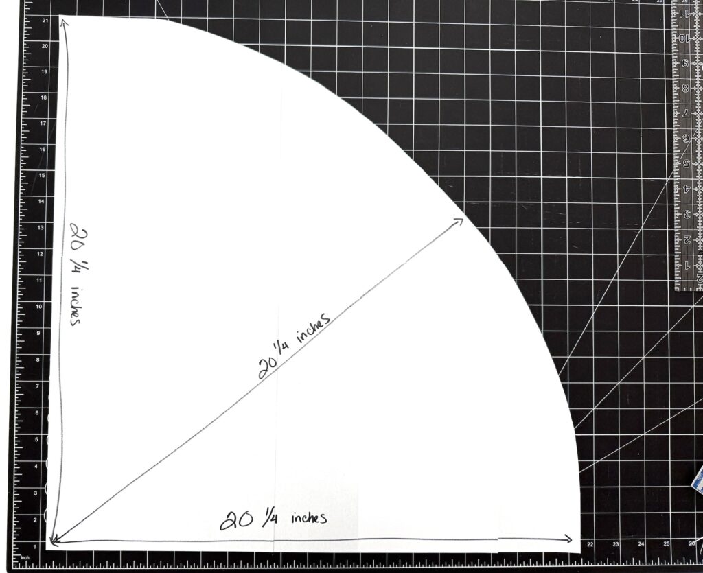 A quarter-circle paper template for an advent tree, with sides and diagonal labeled 20 1/4 inches, placed on a black grid cutting mat with rulers visible along the edges.