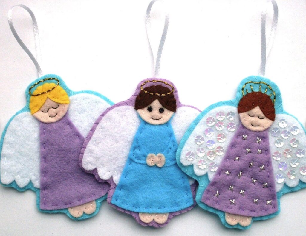 Three handmade felt angel ornaments with white wings, blue or purple dresses, and ribbon loops for hanging are arranged side by side against a white background.