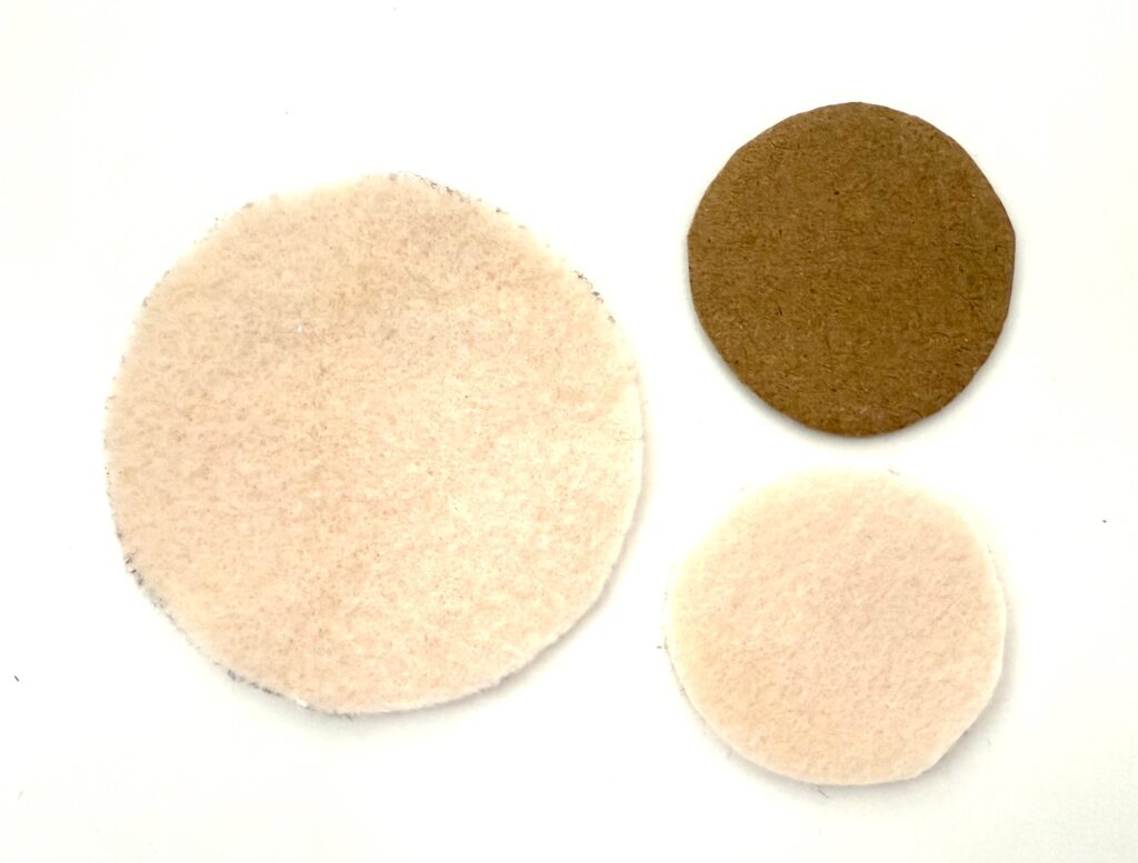 Three round felt circles—one large cream, one smaller cream, and one medium brown—are arranged on a white background.
