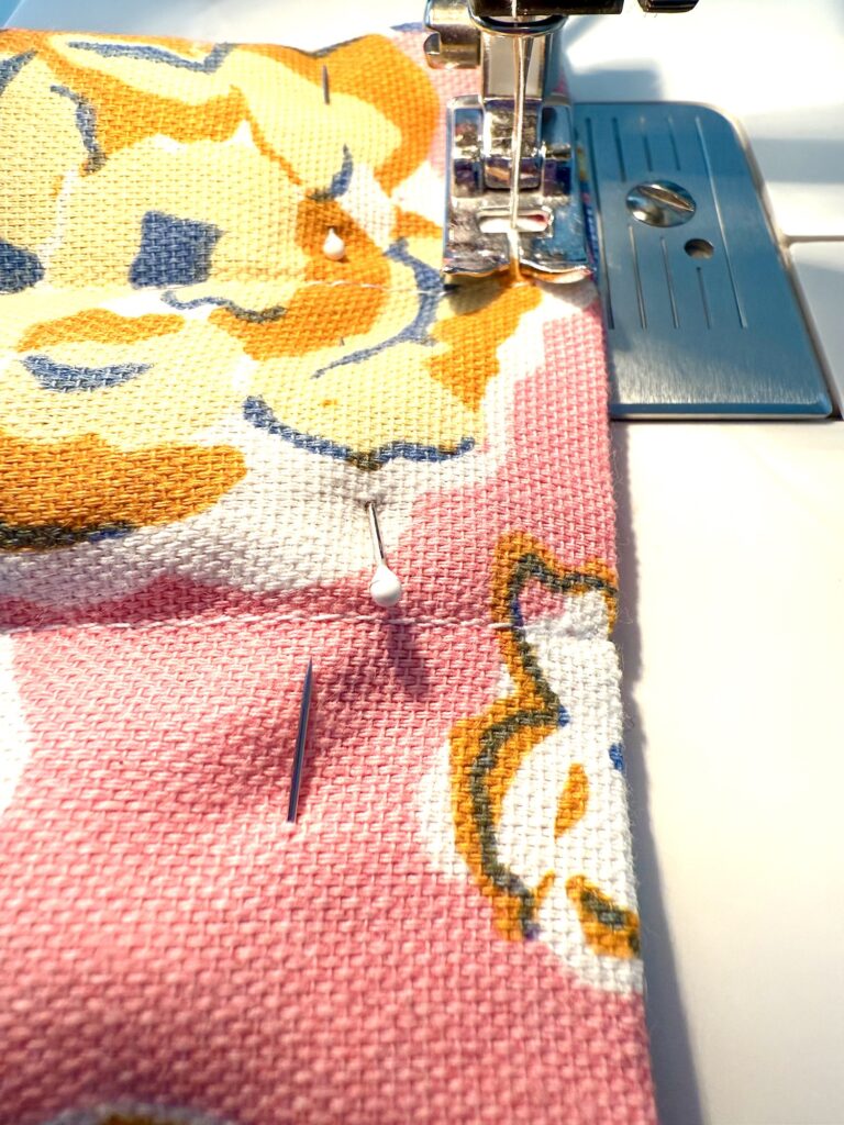 Close-up of a sewing machine stitching floral-patterned fabric, with pins securing the material in place—perfect for crafting a decorative trivet.