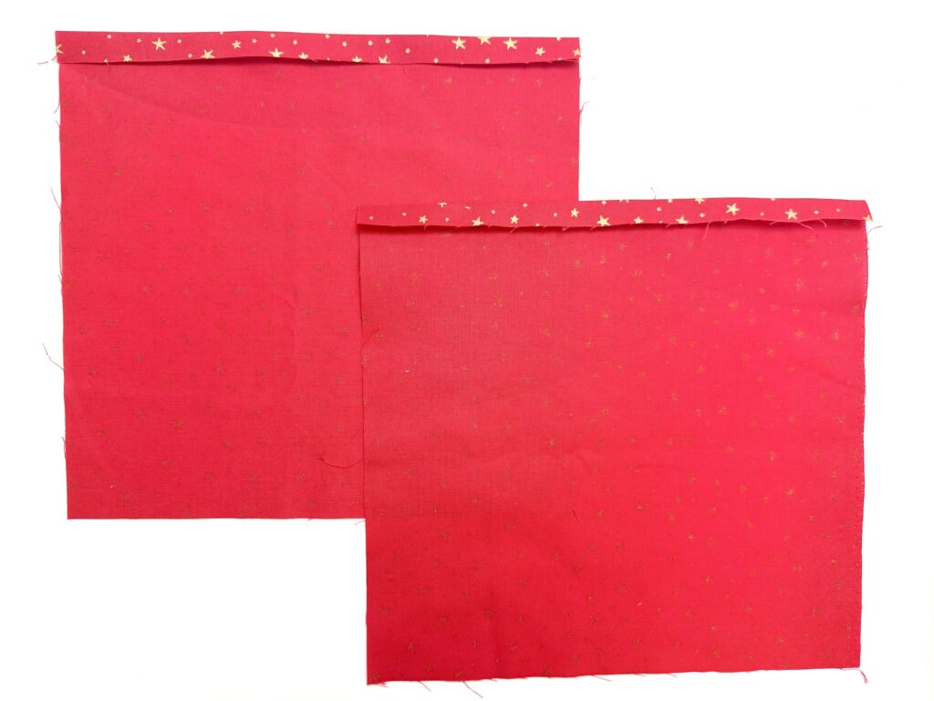 Two red fabric squares with small gold stars are laid flat, each with the top edge folded down and pressed.