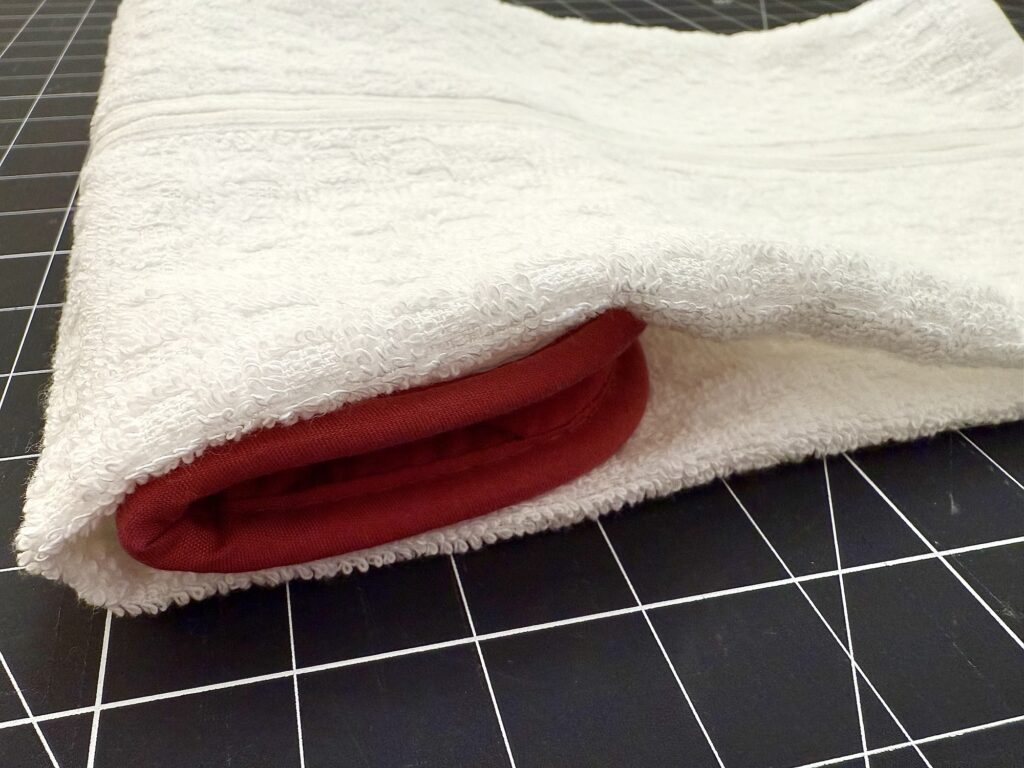 A white towel folded to partially cover a red towel, placed on a black grid-patterned surface.