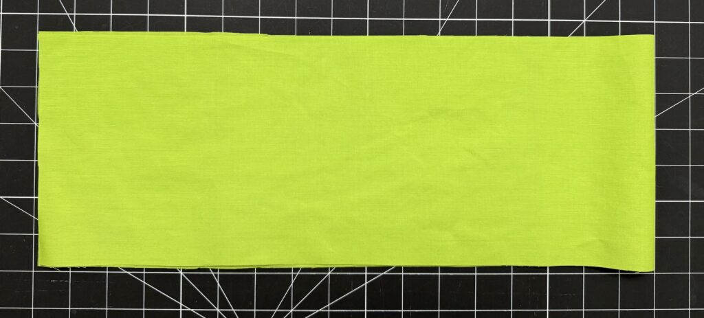 A rectangular piece of bright green fabric, perfect for crafting an advent tree, is laid flat on a black cutting mat with a white grid pattern.