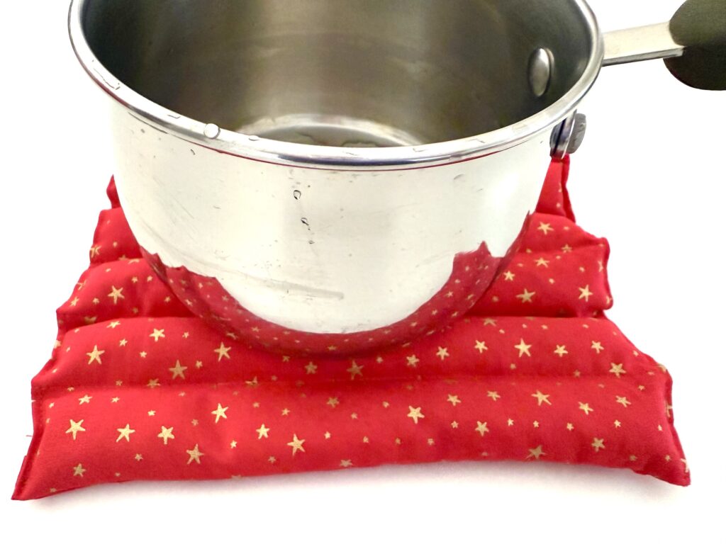 A stainless steel saucepan sits on a red fabric pot holder decorated with gold stars.