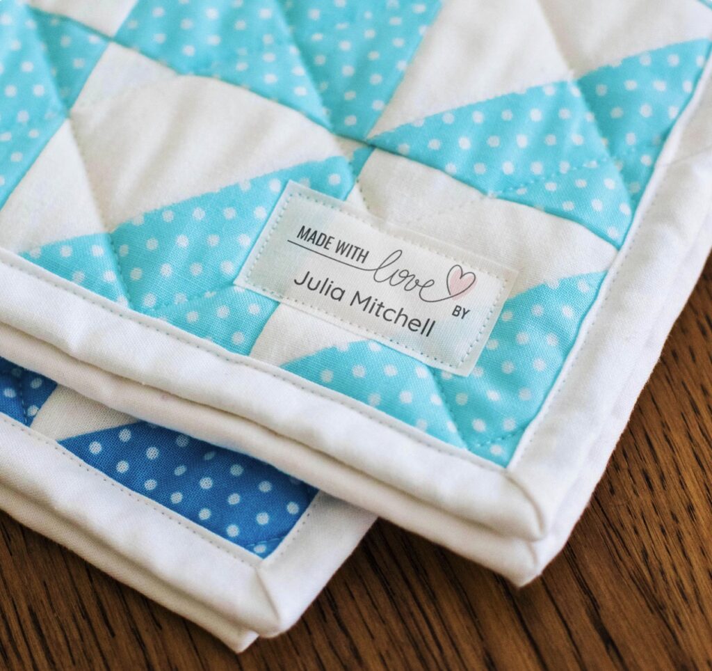 blue and white quilts with a large personalized sewing label sewn on the corner, displayed on a wooden table