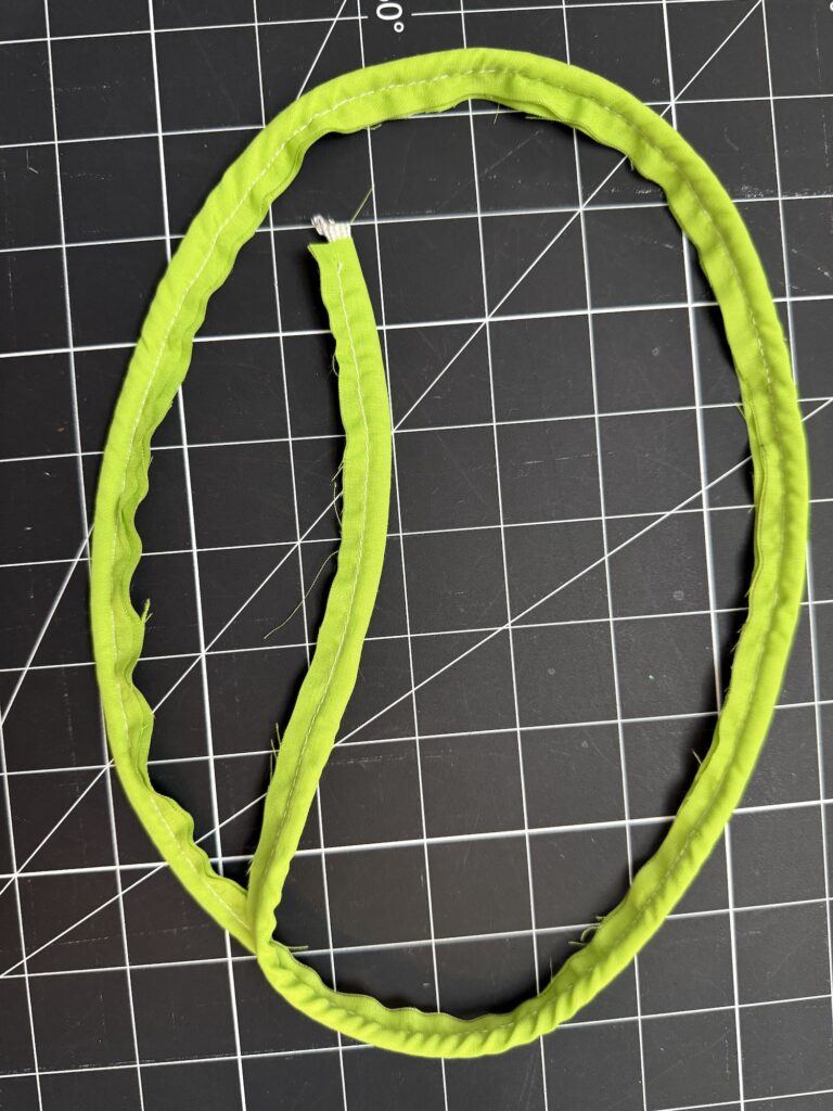 A green fabric tube with one unfinished end, perfect for crafting an advent tree, is laid in an oval shape on a black cutting mat with a white grid.