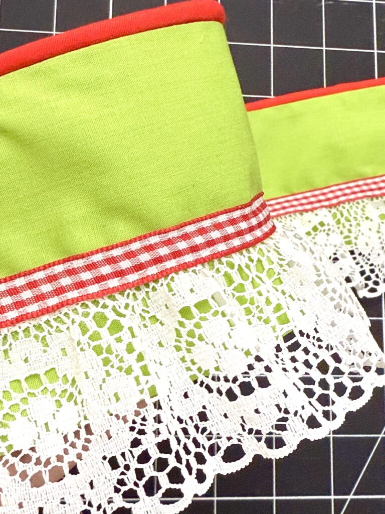 A green cloth advent tree with red trim, red plaid ribbon, and white lace edging is displayed on a black grid background.