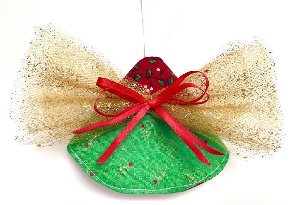 Handmade angel ornament with gold mesh wings, a red bow, and a green fabric dress decorated with small red and green designs, set against a white background.