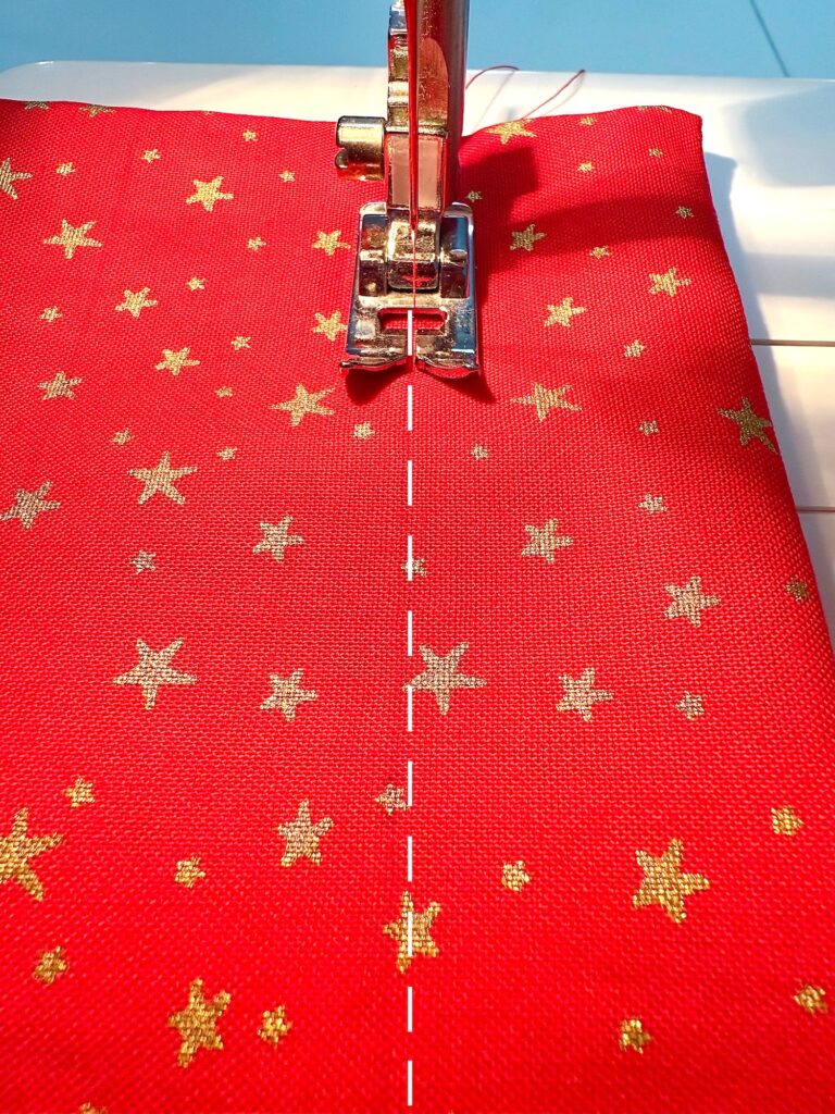 A sewing machine needle stitching along a dashed line on red fabric with a gold star pattern.