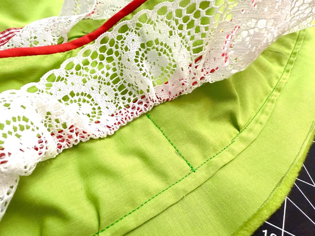 Close-up of bright green fabric with white lace trim and red piping, showing stitching and seam details—perfect for crafting an advent tree.