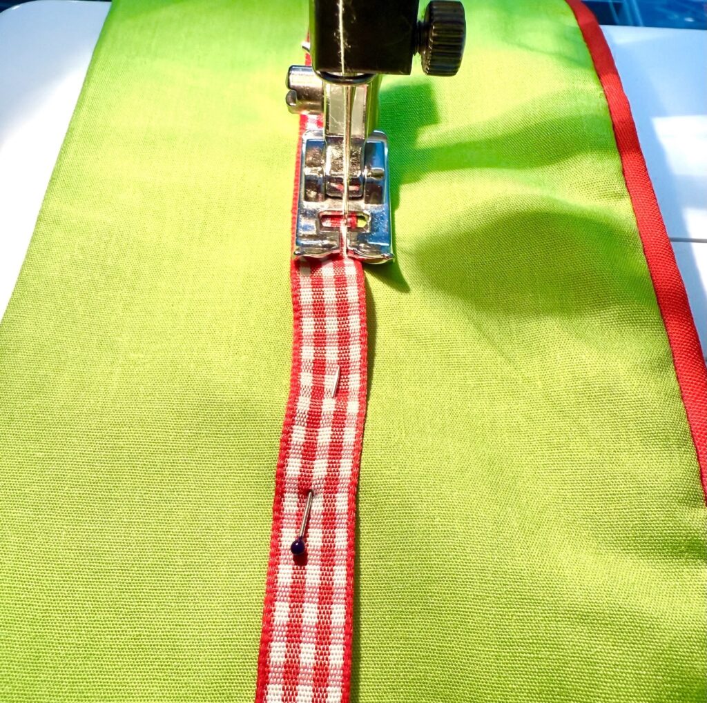 A sewing machine stitches a red and white checkered ribbon onto green fabric with red edging, perfect for crafting an advent tree.