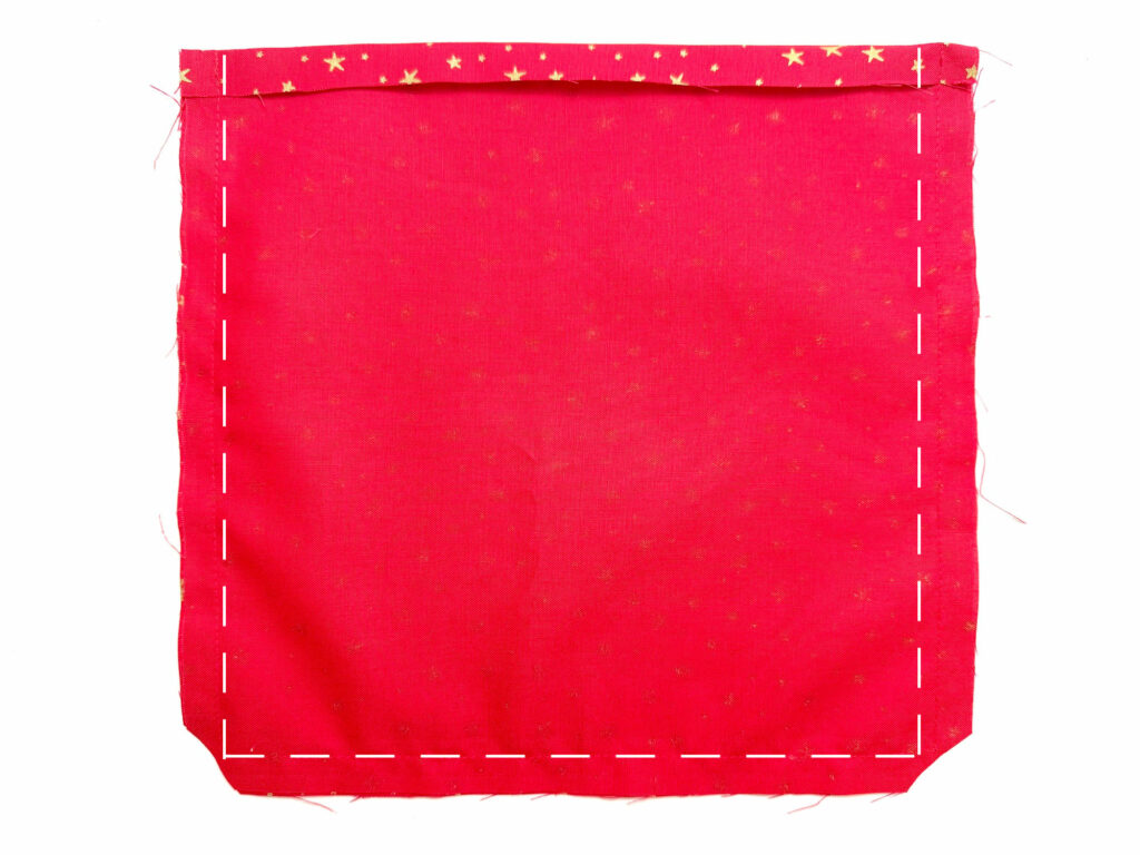 A rectangular piece of red fabric with a folded top edge and dashed white lines marking stitching along three sides.
