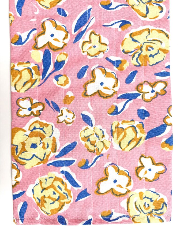 A pink trivet fabric with a pattern of yellow and white flowers, accented by blue and yellow leaves.