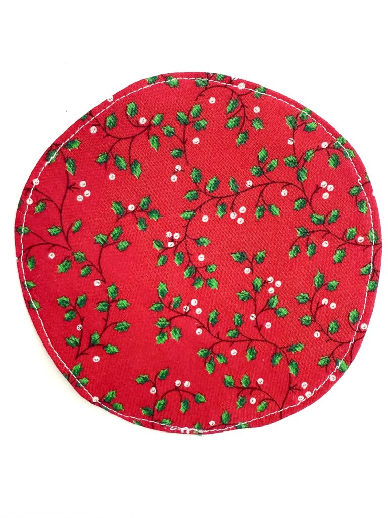 A round red fabric coaster with a pattern of green holly leaves and white berries, set against a white background.