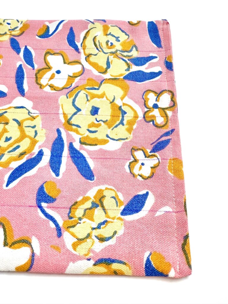 A close-up of pink fabric with a yellow and blue floral pattern, featuring large and small flowers and leaves—ideal for adding a decorative touch to a table trivet.