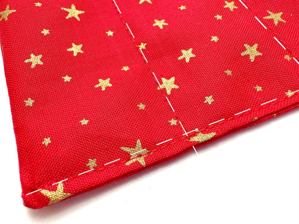 Red fabric with a pattern of gold stars, featuring visible white basting stitches along the edges and a seam line.