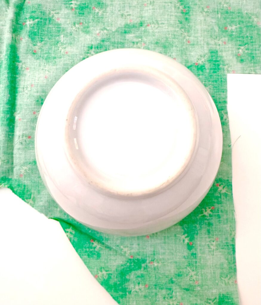 A white ceramic bowl placed upside down on green patterned fabric, next to a piece of white paper.