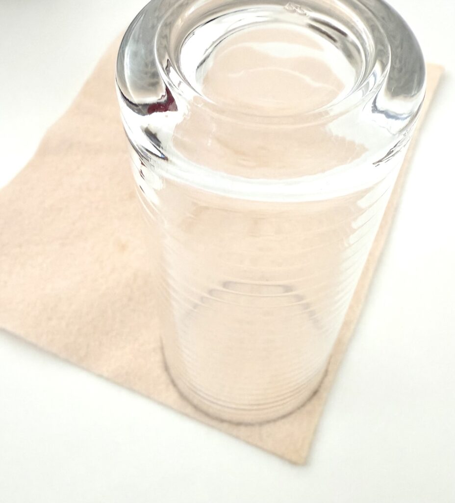 A clear glass is placed upside down on a beige paper napkin on a white surface.