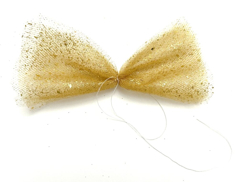 A gold glittery mesh bow is gathered at the center with a piece of white thread on a white background.