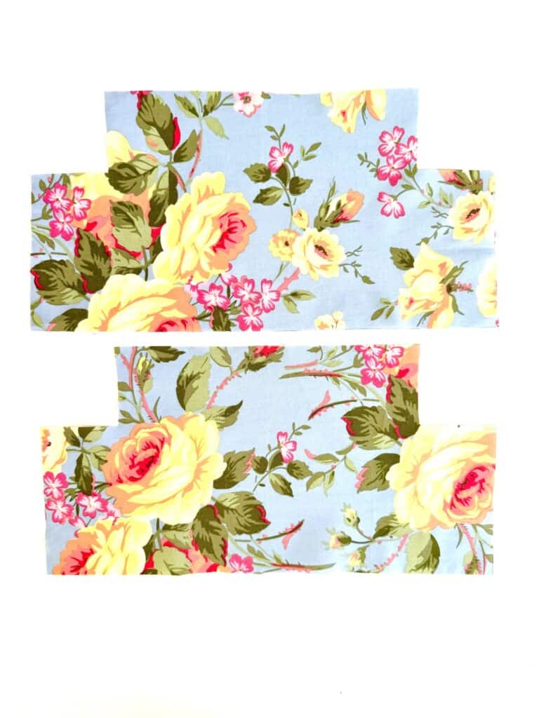 Two rectangular pieces of blue fabric with yellow, pink, and green floral prints, ideal for crafting a charming tissue box cover, are placed on a white background.
