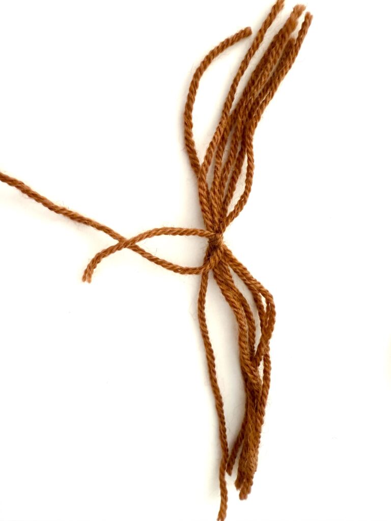 Brown yarn strands tied together in a knot on a white background.