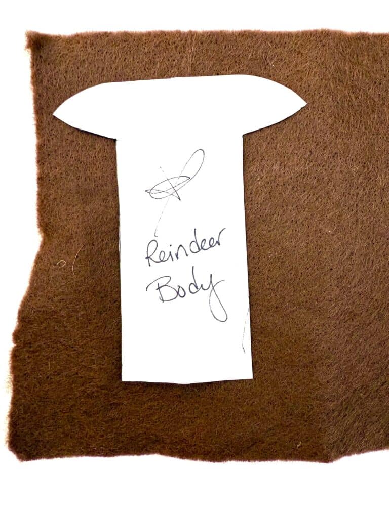 A paper pattern labeled "Reindeer Body" is placed on a piece of brown felt fabric.