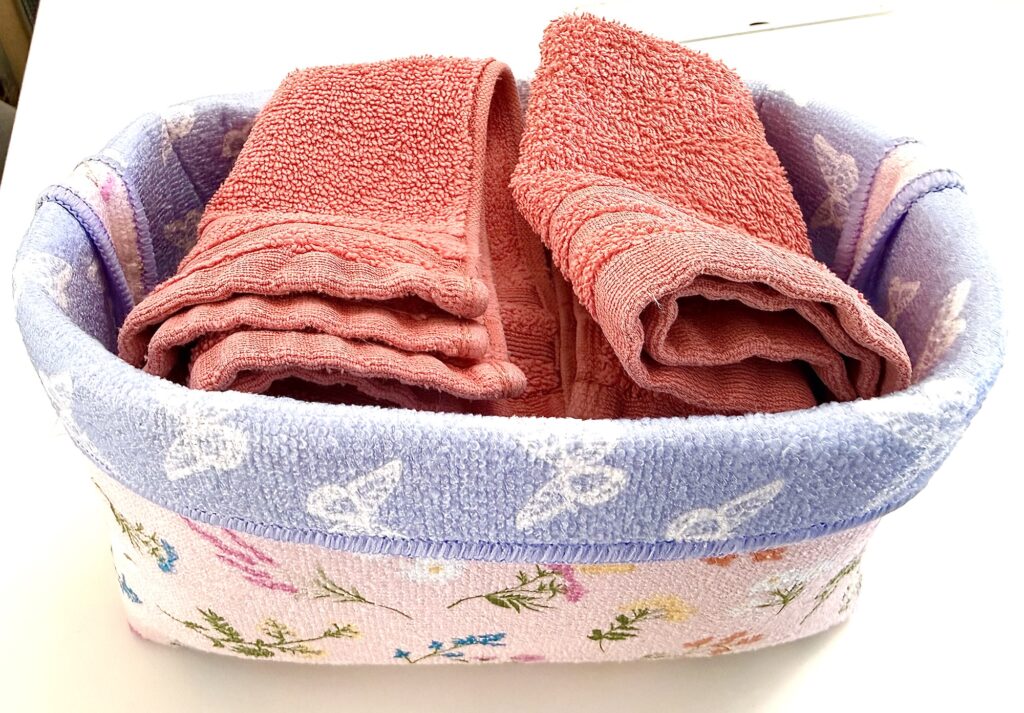 A fabric basket with a floral and butterfly pattern holds two neatly folded pink towels.