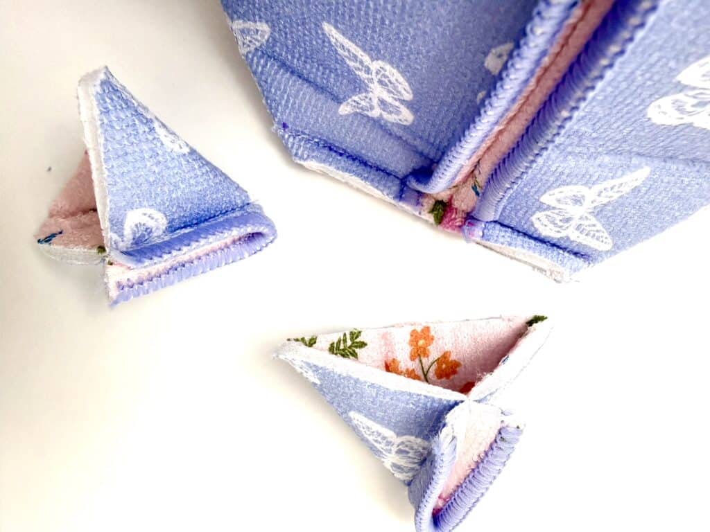 Close-up of fabric pieces with purple and pink floral patterns, some folded into triangles, on a white background.