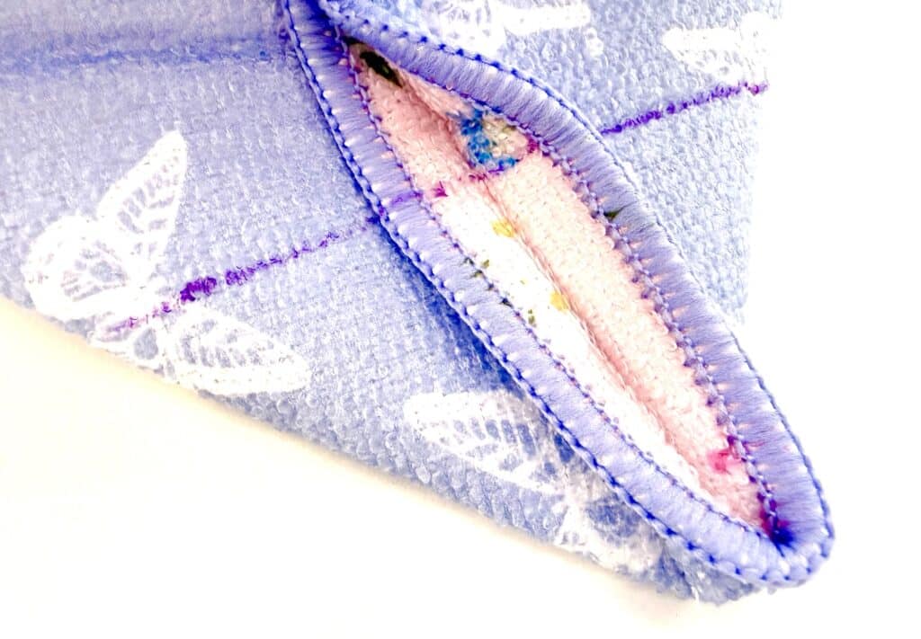 Close-up of a folded, reusable cloth pad with a purple and white butterfly pattern, showing pink absorbent inner layer and purple stitching.